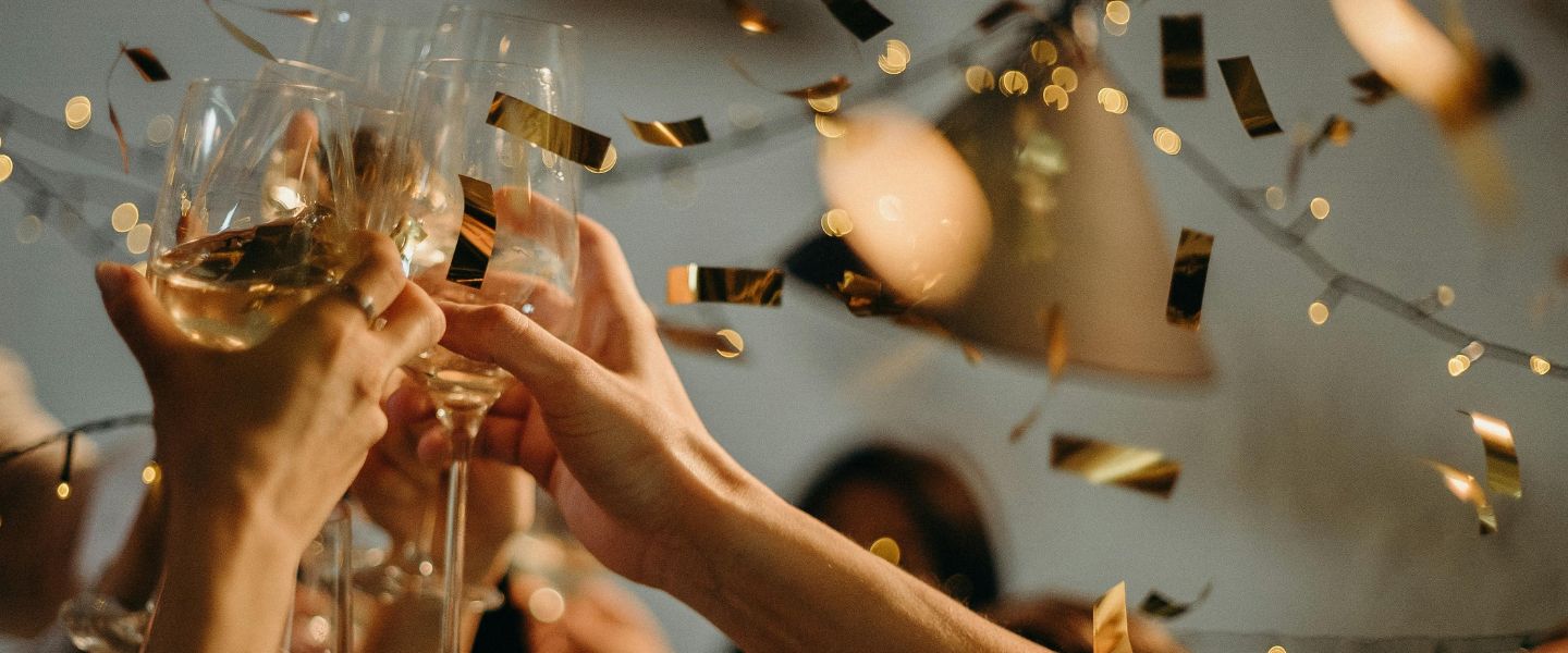Hands touching glasses together in a room full of gold confetti