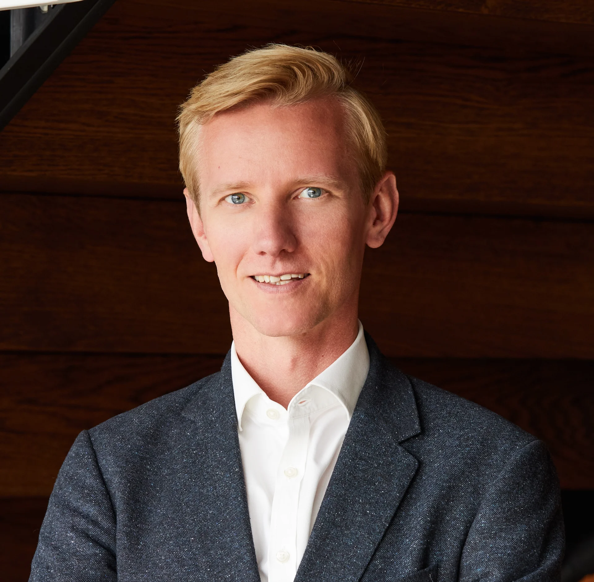 Headshot of Oli Knight, Head of Workplace at Landsec. A man in professional attire with a dark wood wall in the background.
