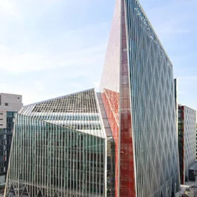 Exterior view of a dramatically designed **modern glass building** with sharp geometric lines and a striking vertical red glass fin, likely **Nova, Victoria** or a similar landmark.