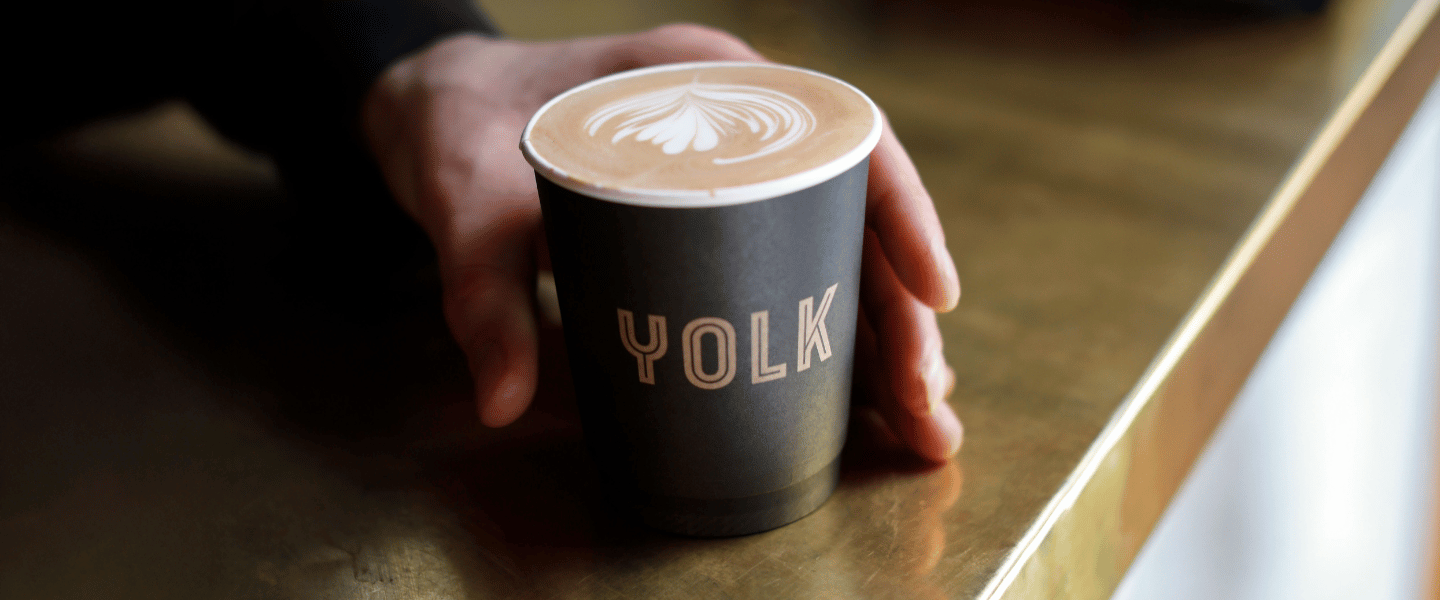 A hand reaching out to pick up a Yolk coffee cup