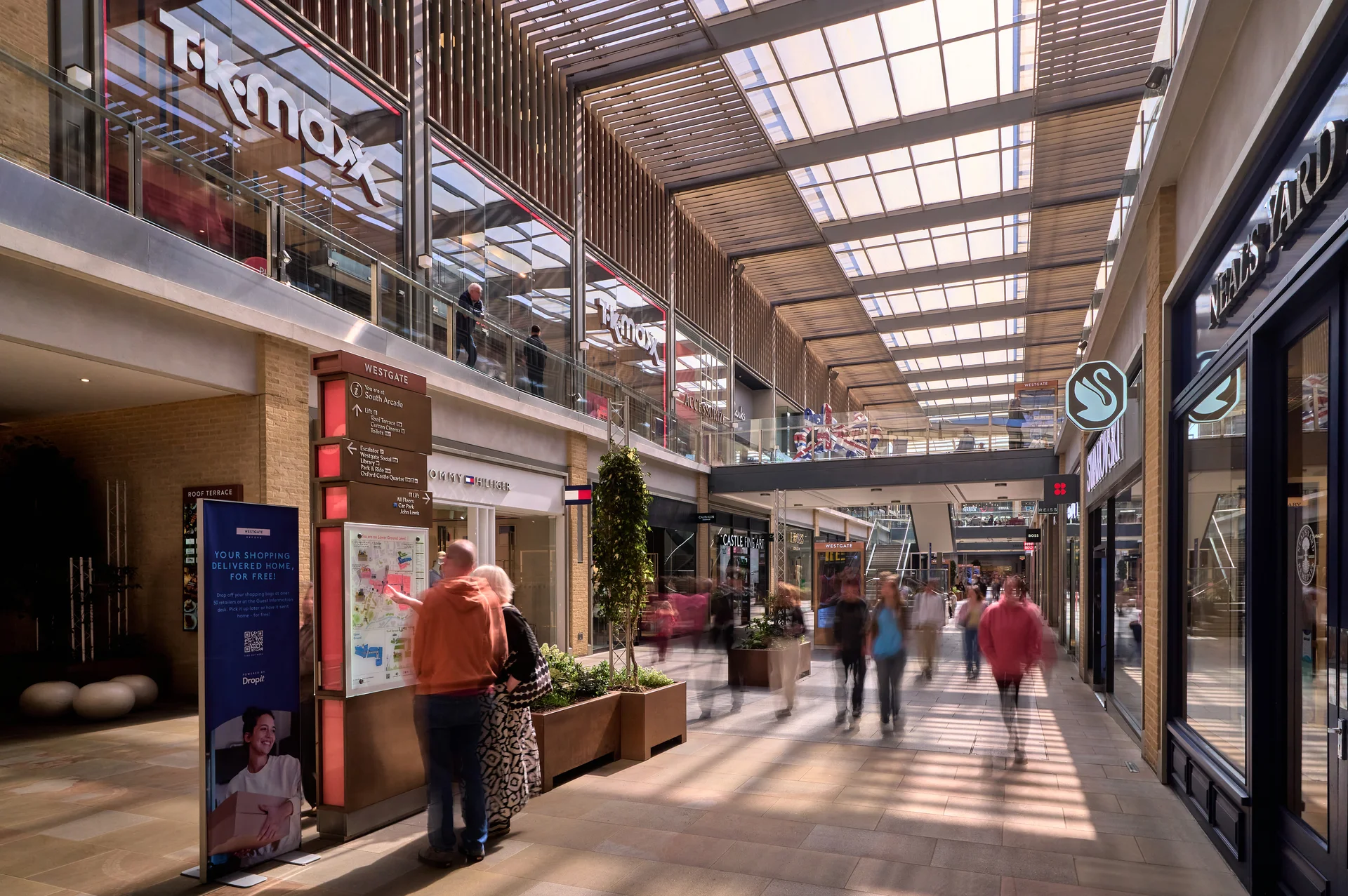 Westgate Oxford mall interior with TK Maxx and Tommy Hilfiger. Shoppers consult a directory under a slatted roof.