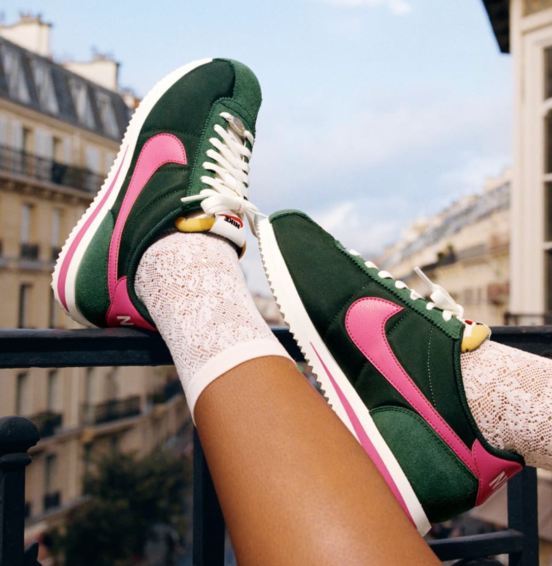 A pair of woman's legs wearing green Nike trainers, resting her shoes on a balcony ledge.