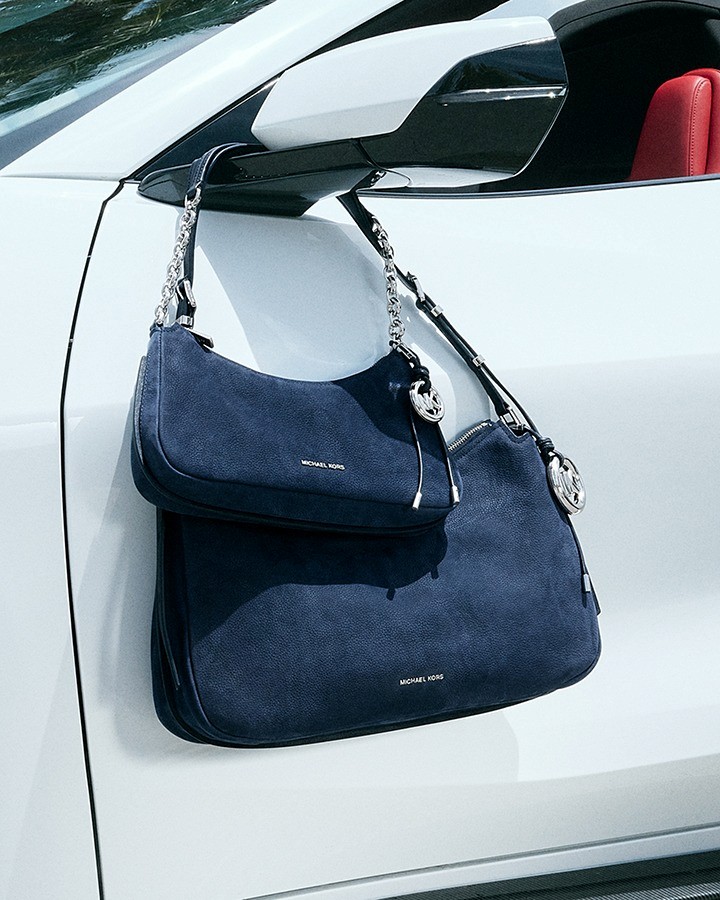 Two dark blue Michael Kors handbags hang from a white car's wingmirror.
