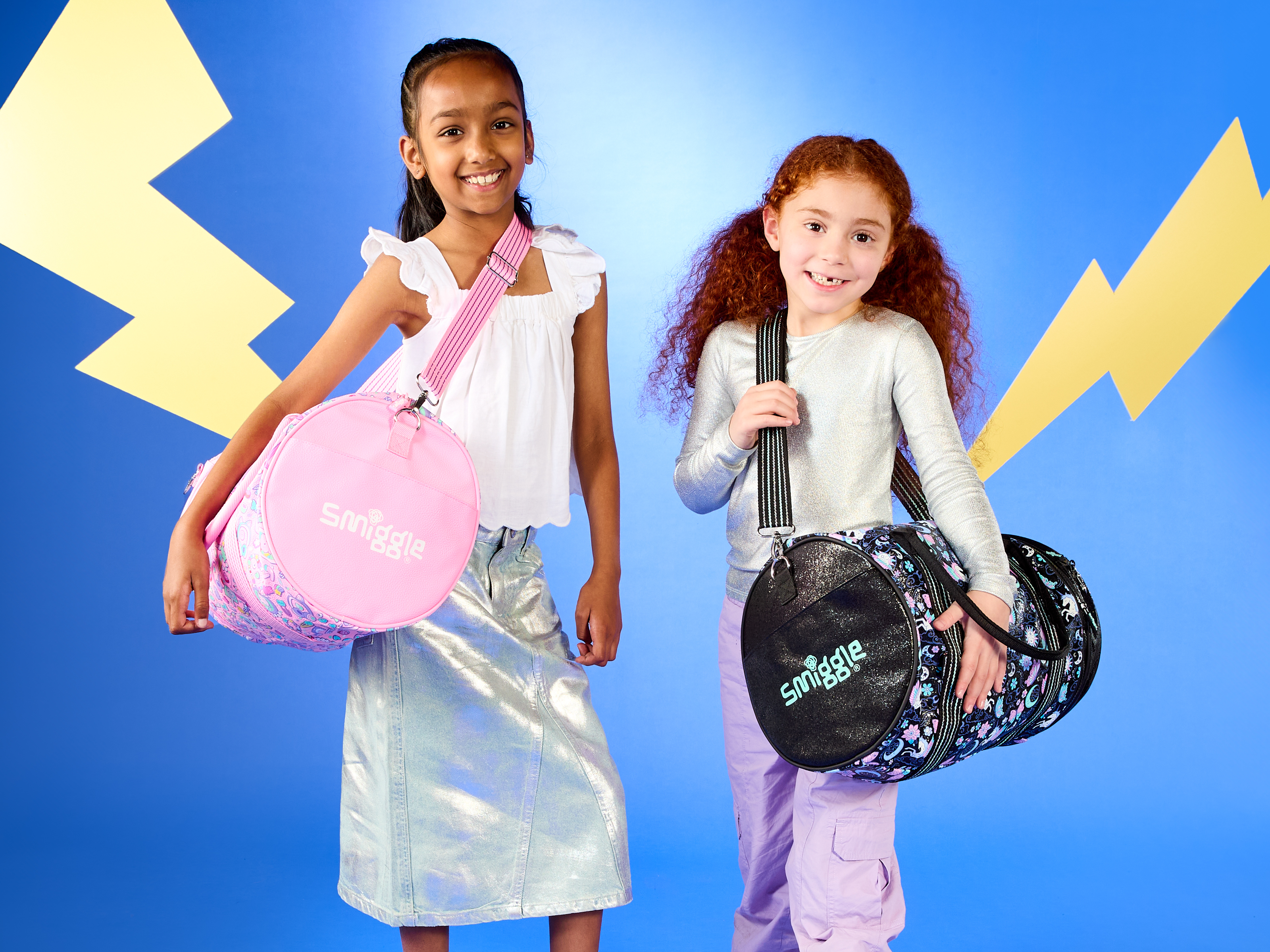 Two young girls with Smiggle bags in front of a blue and yellow lightning graphic backdrop