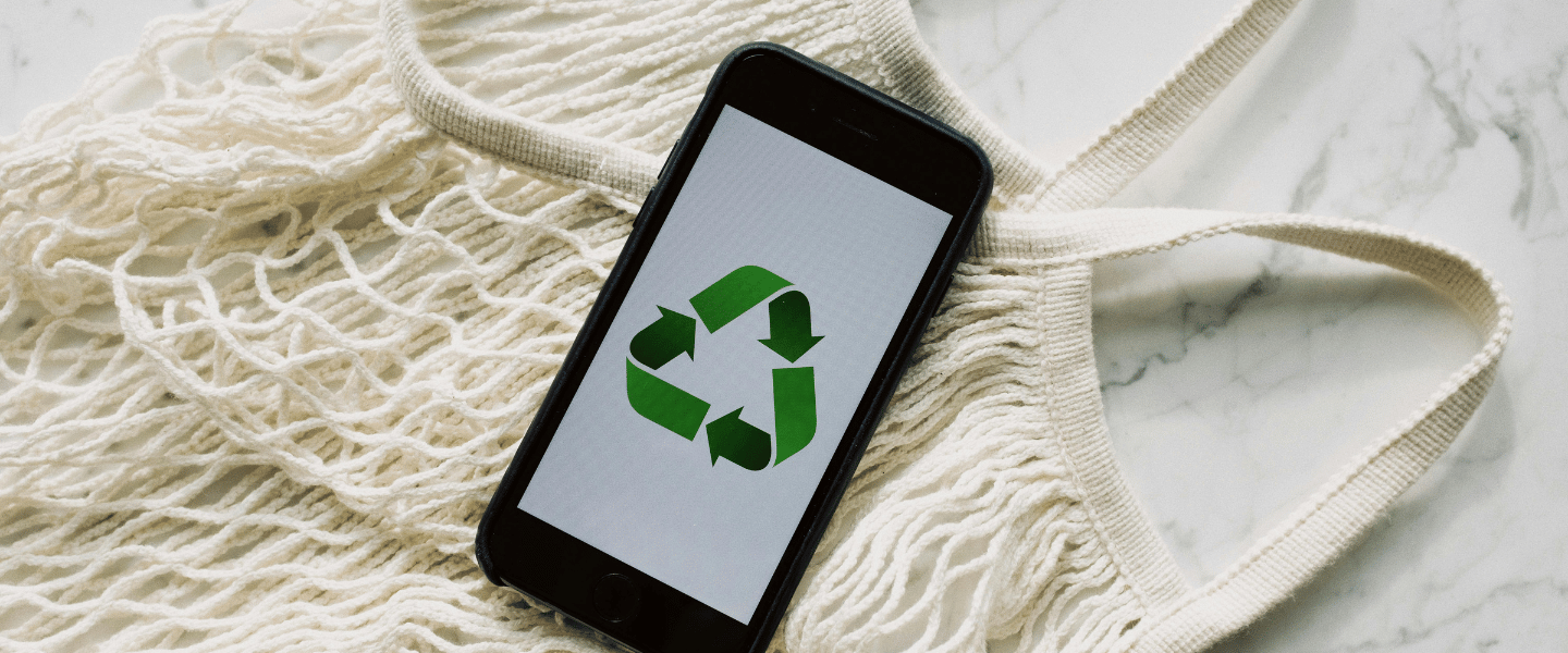 A phone on top of a string bag with a green recycling icon on the screen