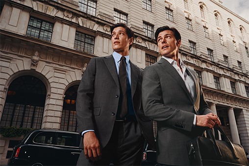 Two men in suits wait outside for a taxi