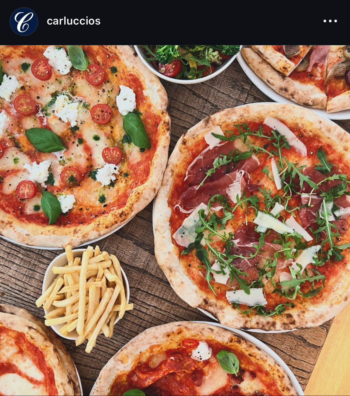 A selection of pizzas on a wooden table with some fries and a side salad in small bowls 