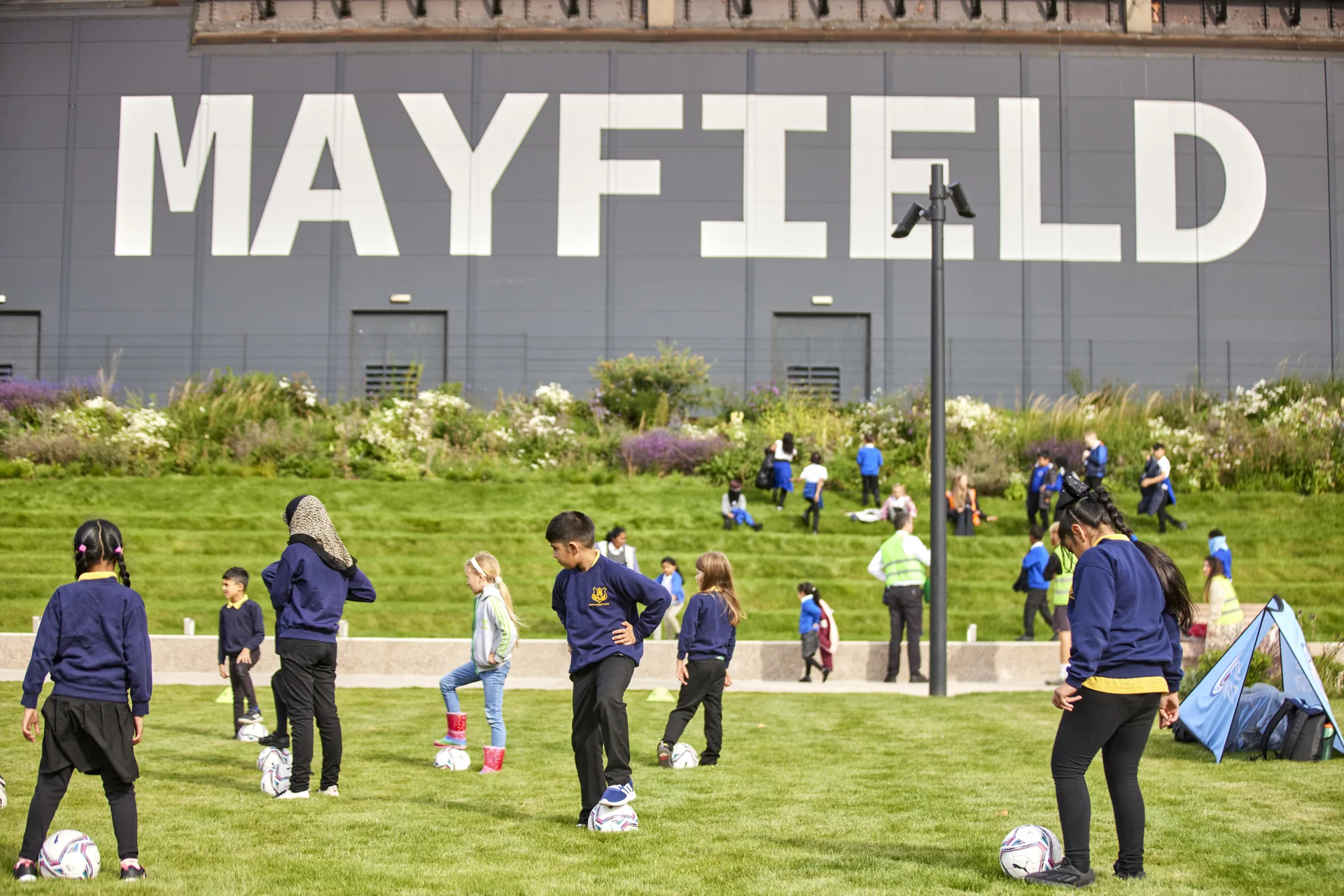 Children playing football on a grassy field near a "MAYFIELD" sign.