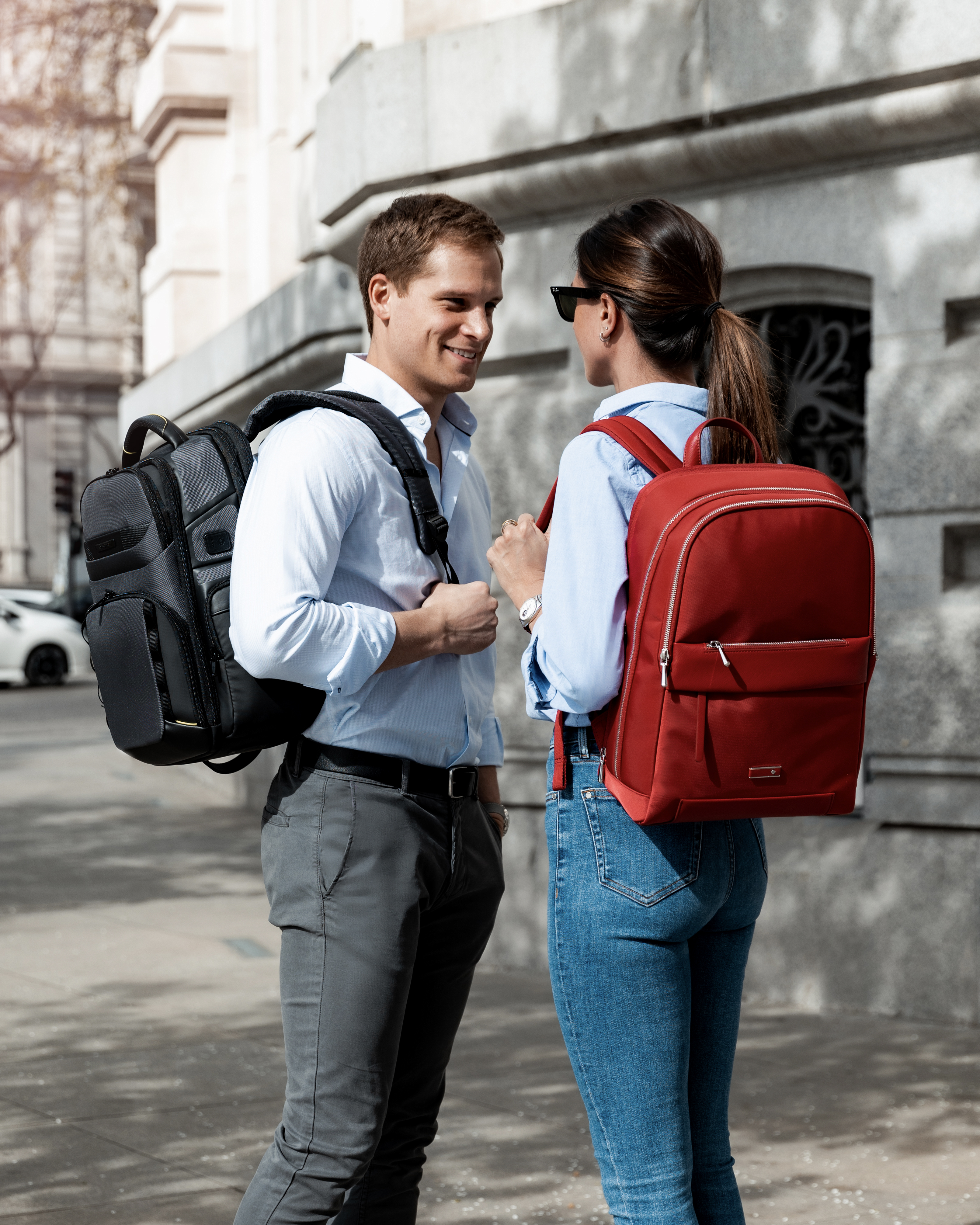 A man and woman speak together in the street both wearing smart backpacks
