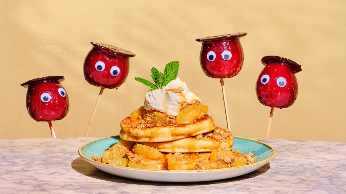 A stack of pancakes surrounded by apples on sticks