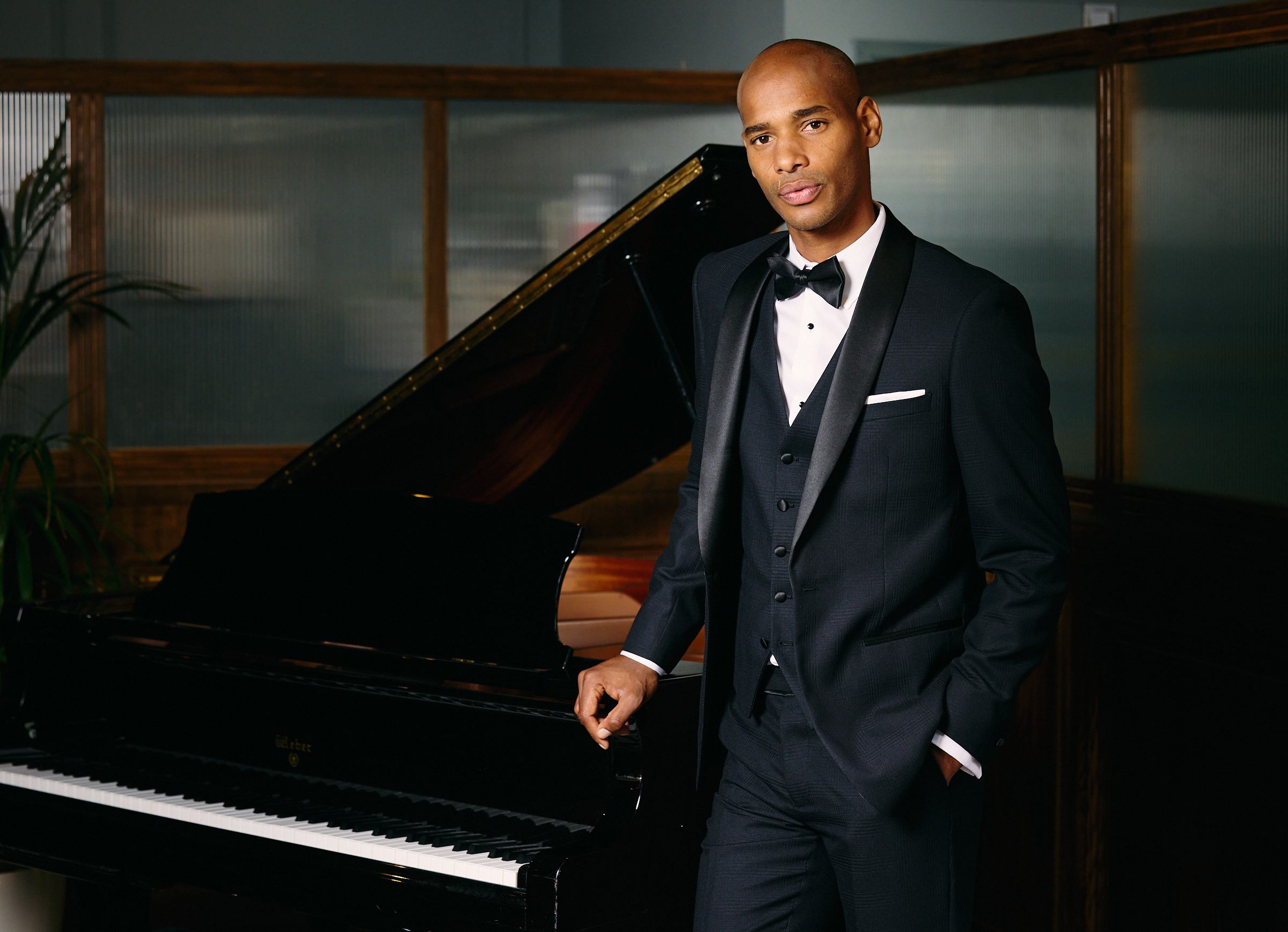 A man in a suit leans on a grand piano