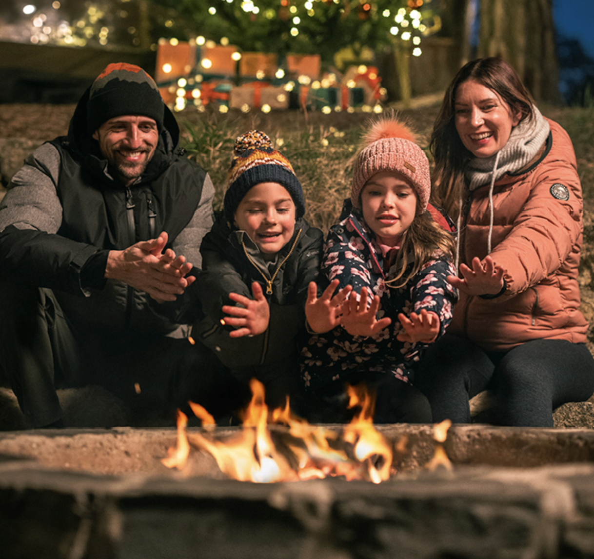 A family warm their hands around a fire outside at Christmas
