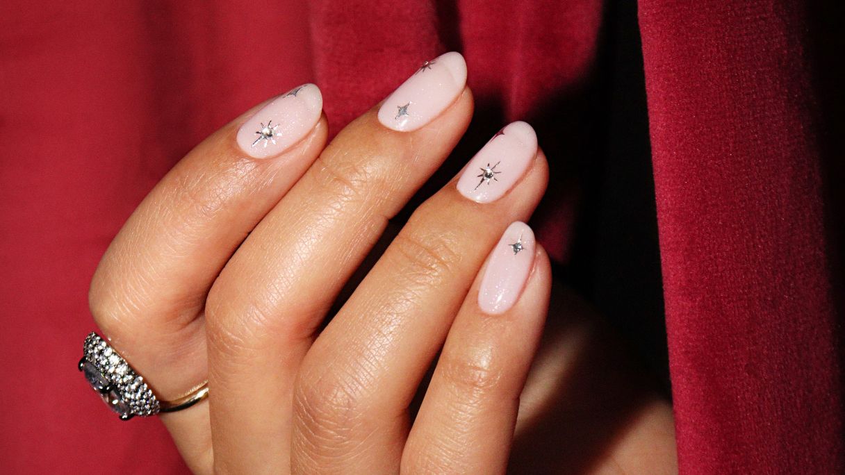 A hand with silver nail art against a red velvet curtain