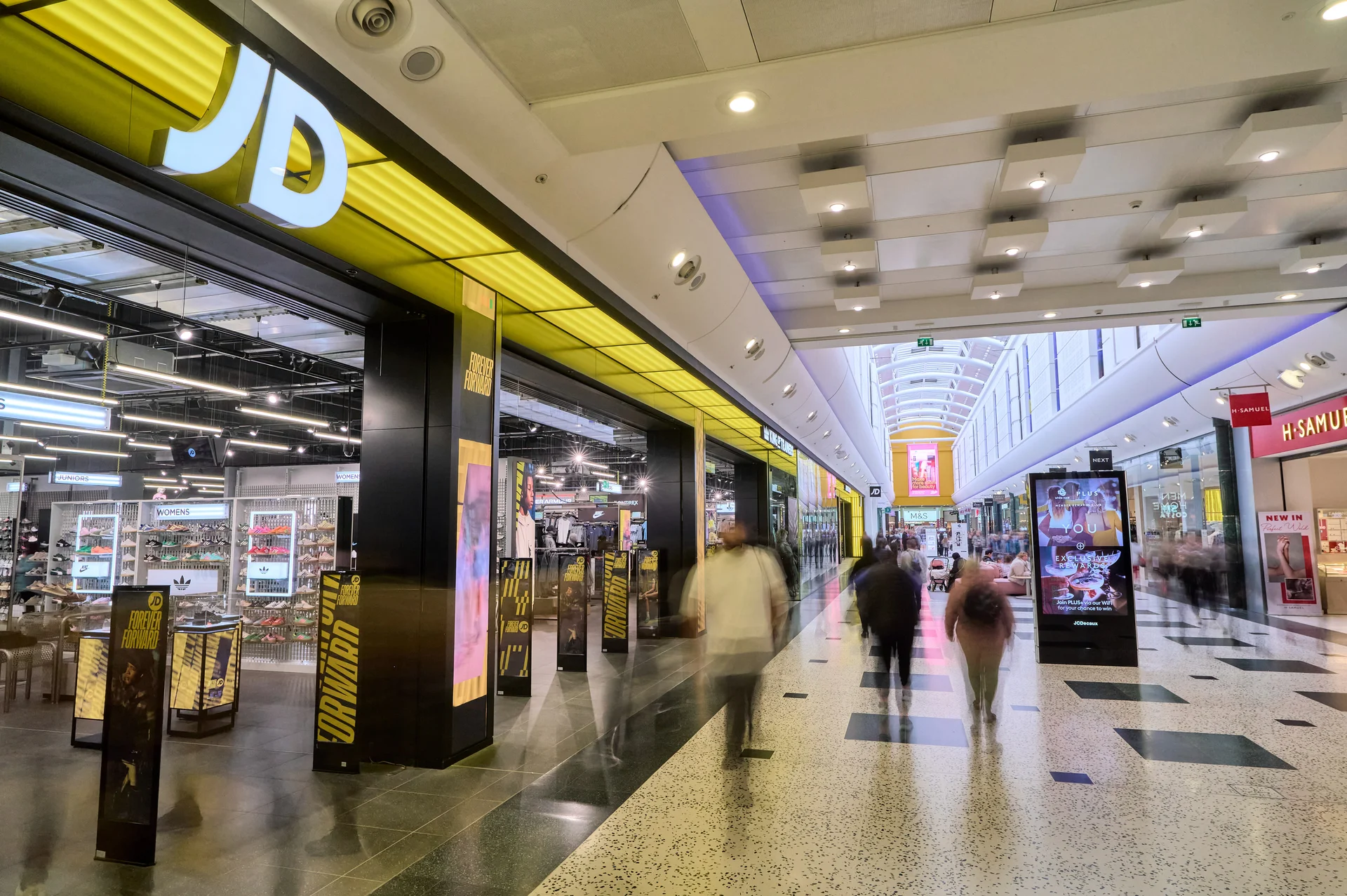 Interior view of the **White Rose Shopping Centre** mall, showcasing the large entrance of the **JD Sports** store with its bold yellow signage, and shoppers walking down the brightly lit corridor.